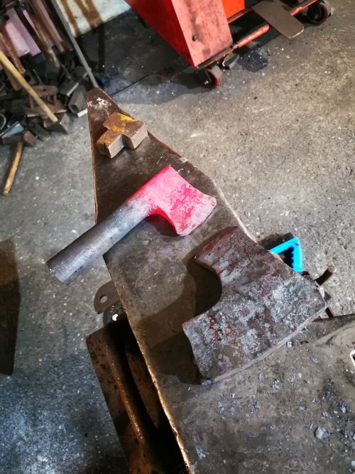 Hache en cours de formage, posée sur une enclume, le fer rougeoyant