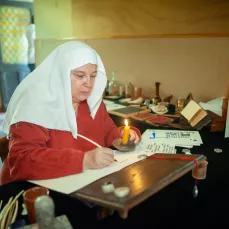 Dame Chlodyne calligraphiant avec une plume à Pérouges en 2018