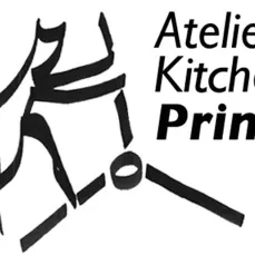 Un chat debout sur ses pattes arrières. Il est stylisé (simplifié) et il actionne les bras d'une presse pour la gravure avec ses deux pattes avant. Il est écrit à côté "Atelier Kitchen Print"