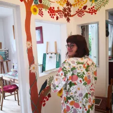 Marie Hardy devant une fresque murale représentant un arbre de vie