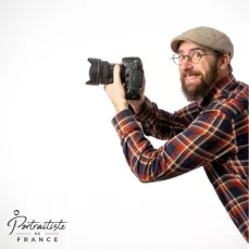Auto-portrait de Henri Derus, portraitiste de France, apparaissant de profil et souriant par le coté droit de l'image, tenant un appareil photo entre ses mains.