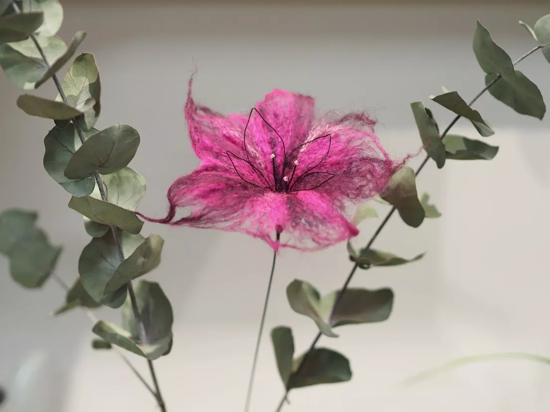 Fleur délicate en laine feutrée et soie, tons de roses, entourée de branchages d'eucalyptus