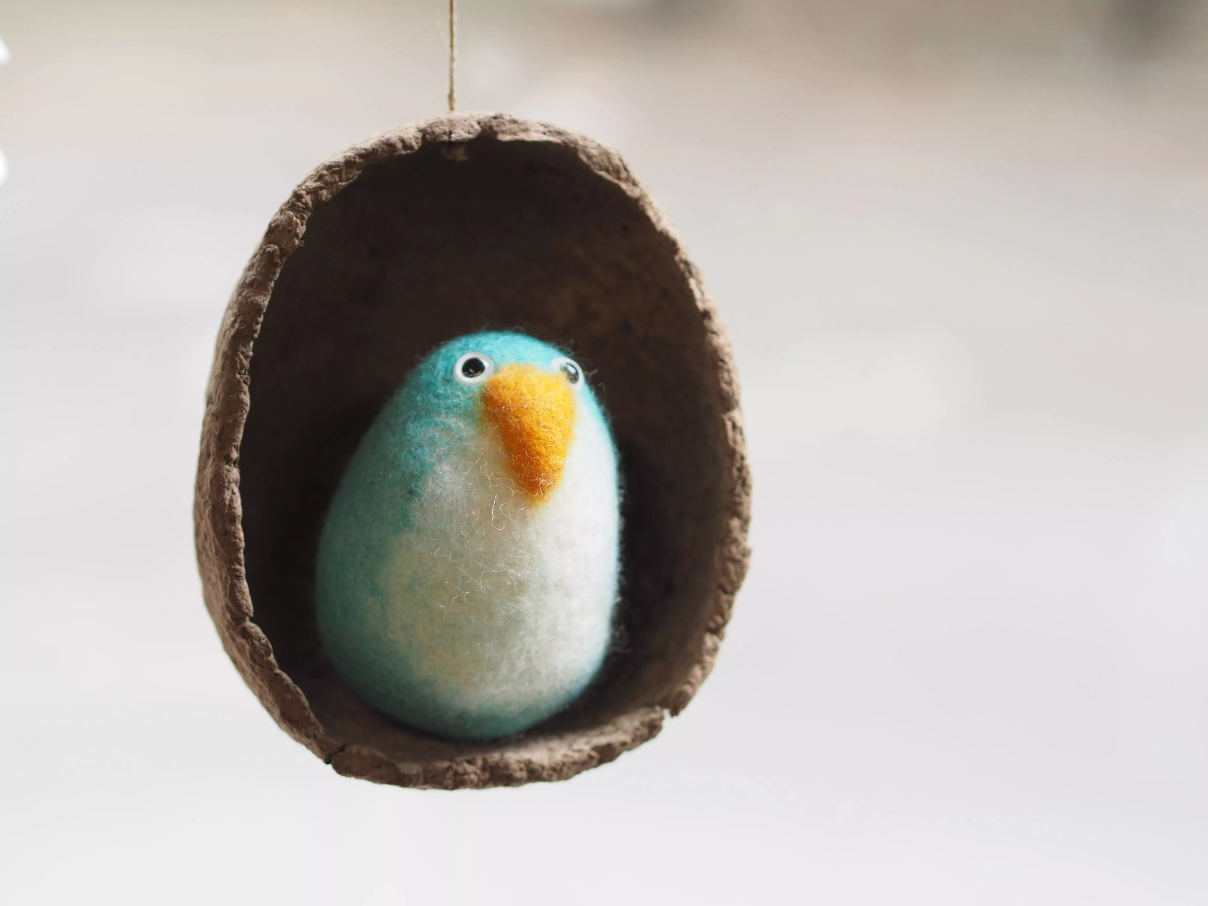 Petit pingouin bleu turquoise dans un cocon ovoïde suspendu réalisé en papier maché