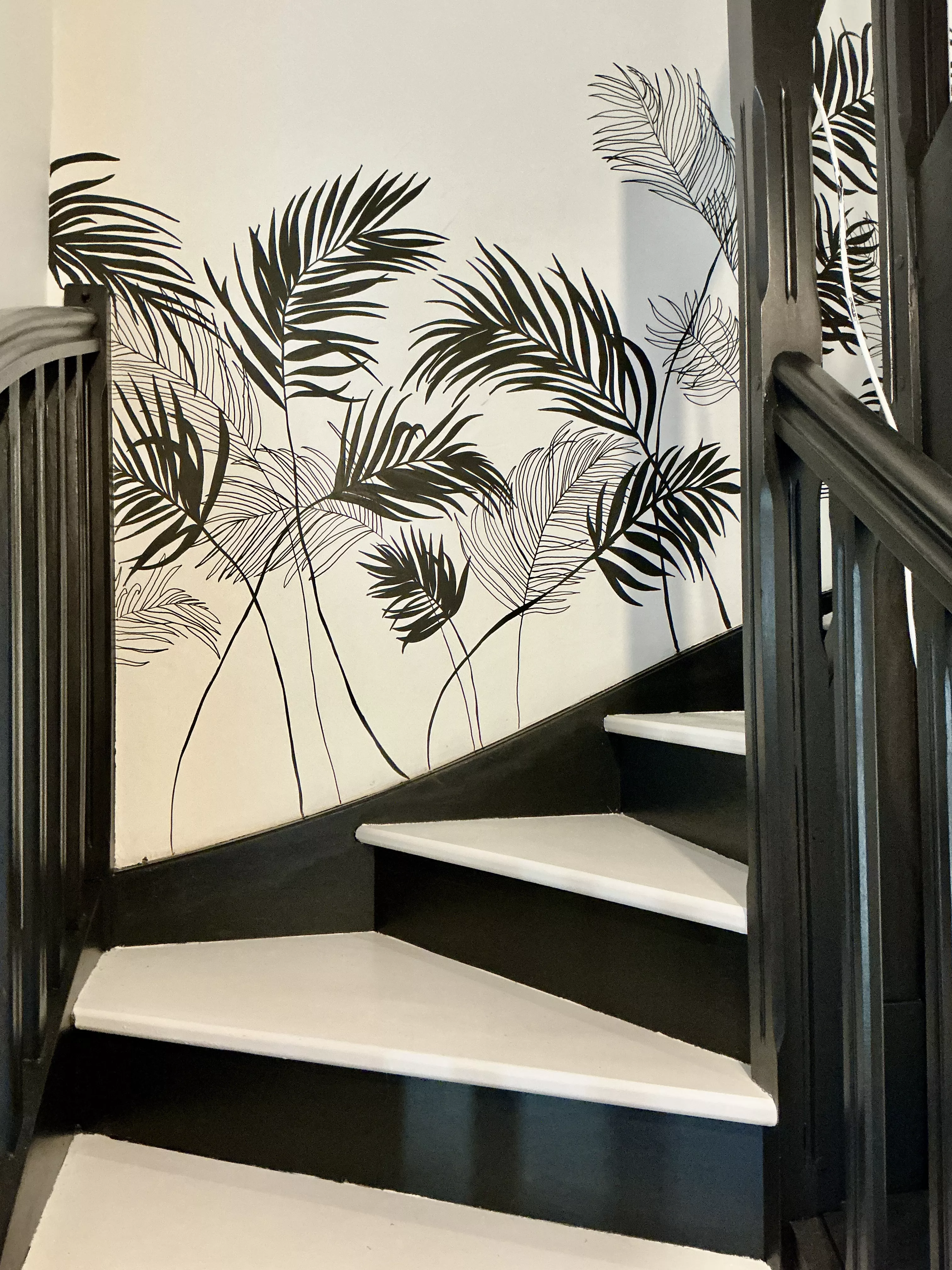 Fresque en noir et blanc dans une montée d'escalier représentant des ombres de feuilles de palmier