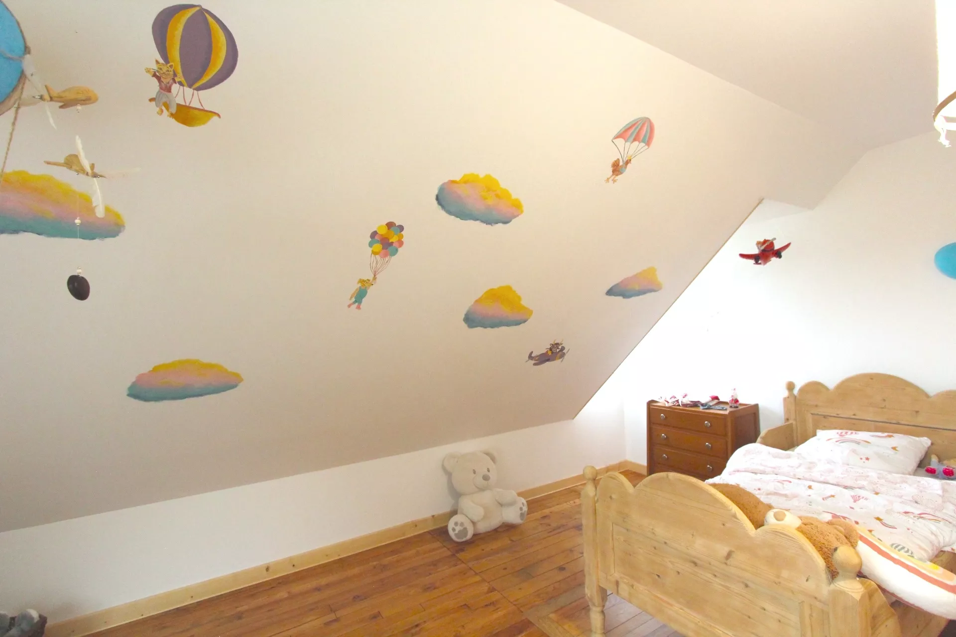 Fresque sur le mur en sous-pente d'une chambre d'enfant en Normandie, représentant un ciel avec des nuages et des animaux dans des engins volants,