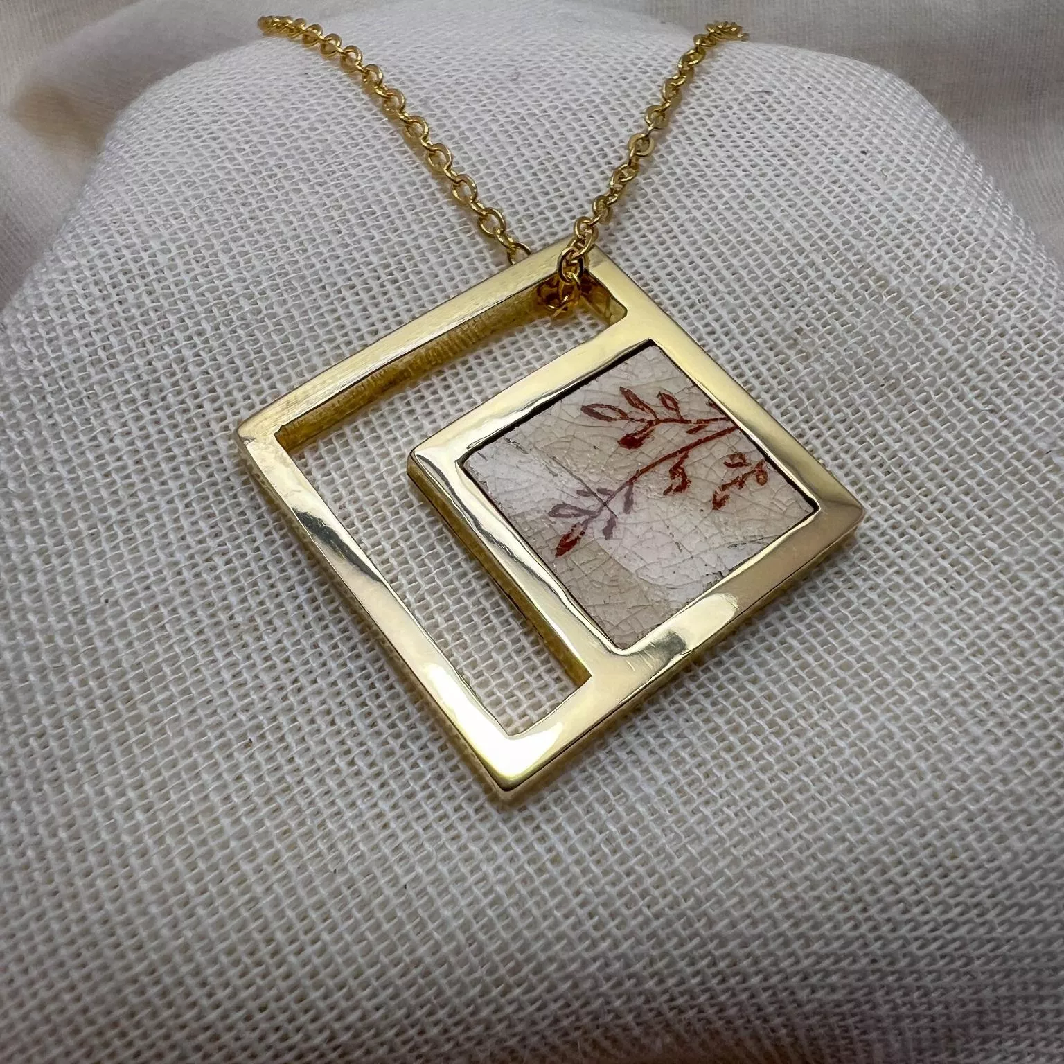 Pendentif carré en laiton doré avec fragment de faïence ancienne à motif floral, monté sur chaîne.