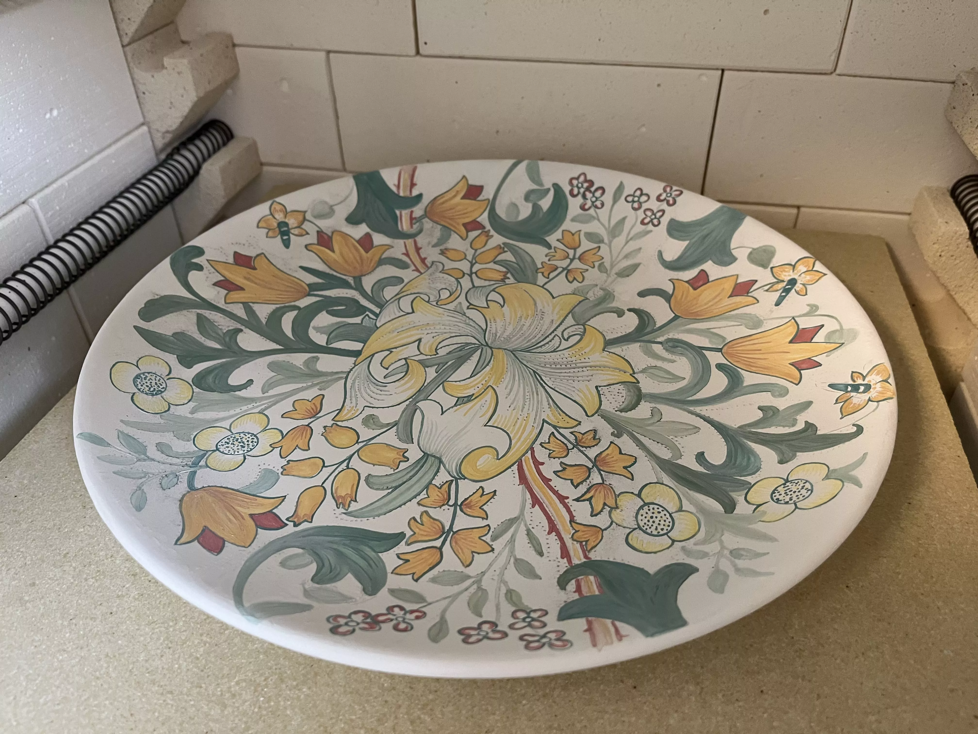 Grand plat de 30cm de diamètre. La photo montre le plat déposé dans le four électrique spécifique pour la cuisson céramique. On peut voir le plat recouvert d'un émail blanc opaque, la peinture a été réalisée sur cet émail encore poudreux. La cuisson à 980 degrés va permettre la fusion du décor peint et de l'émail. 