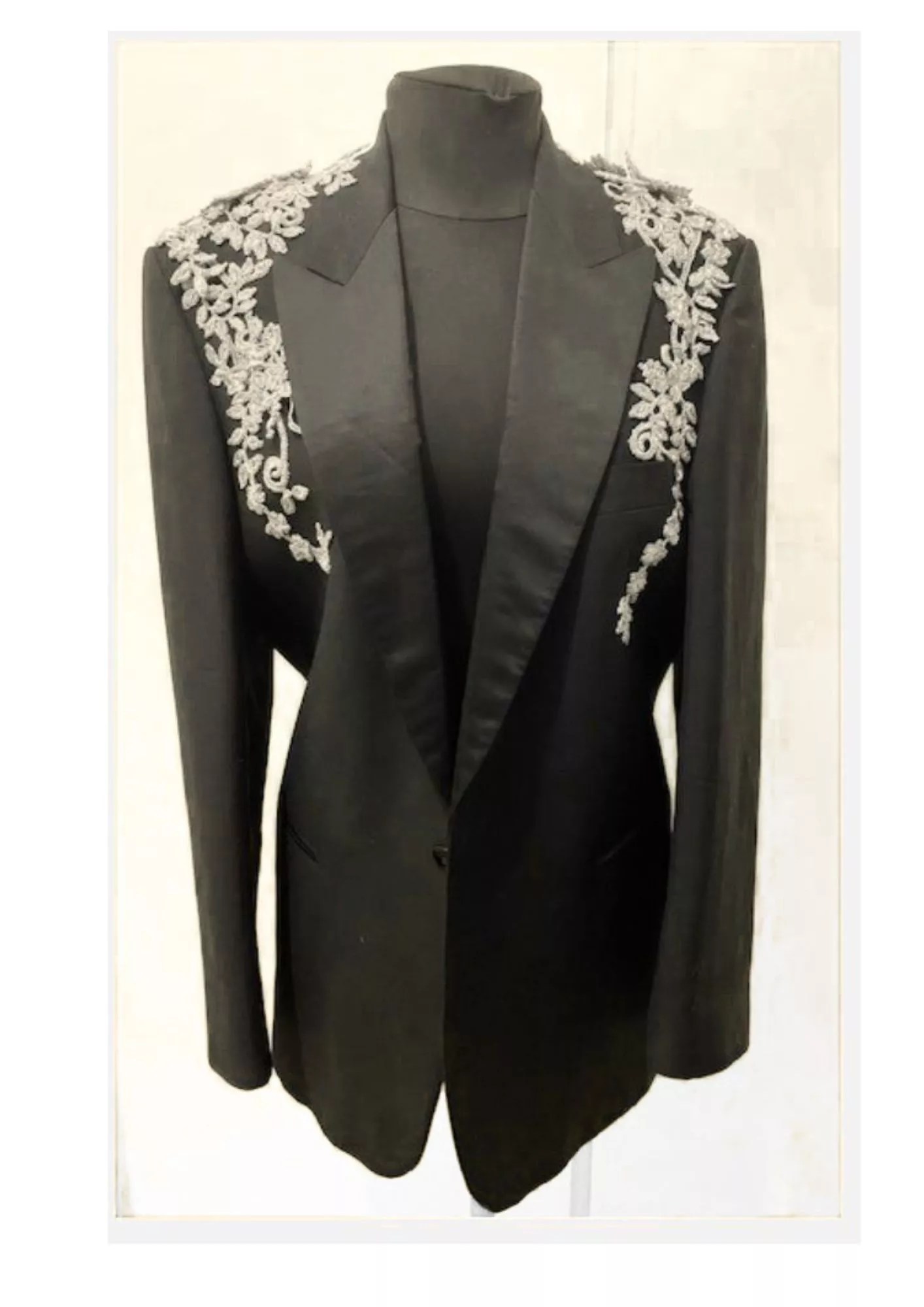Veste de smoking agrémentée de fleurs argentées en crochet, entièrement réalisées à la main. Les motifs ornent les épaules et le haut du buste avant de se prolonger en délicates arabesques le long des côtés de la veste.