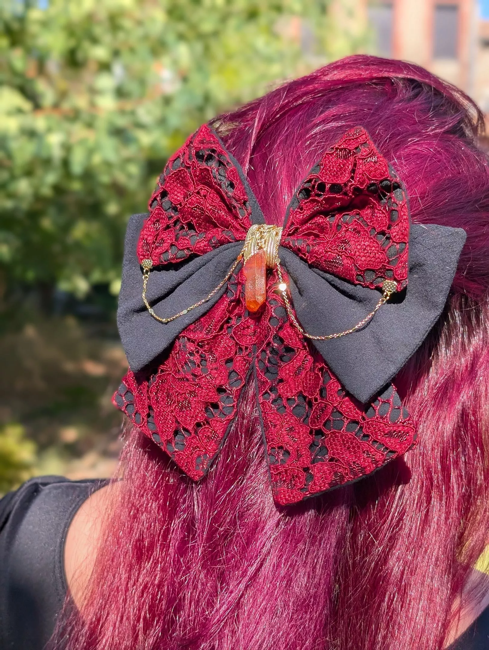 Grand nœud pour cheveux noir et rouge en dentelle, décoré d’une chaîne dorée et d’un cristal, porté en demi-queue.