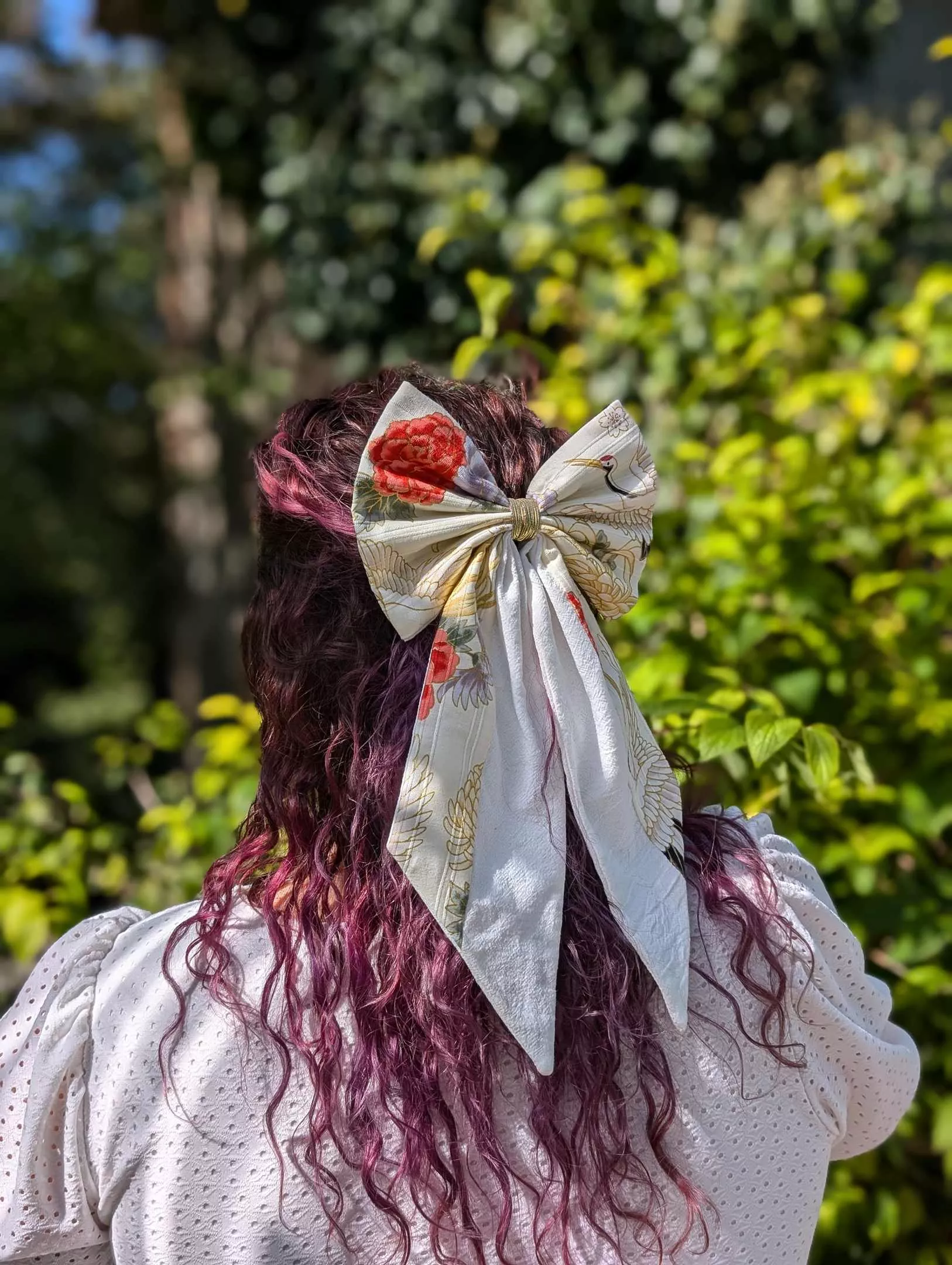 Grand nœud japonais blanc à motifs de grues et fleurs rouges, porté sur cheveux longs en demi-queue.