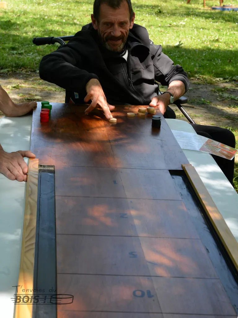 Une personne âgée en fauteuil joue au jeu de galet, un jeu fabriqué en bois de récupération par T'envoies du Bois ! Photo prise lors d'une animation de jeux en bois à Toulouse.
