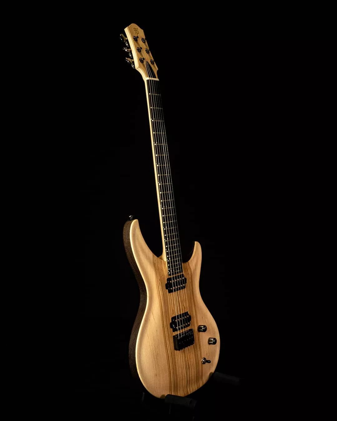 Guitare électrique à manche traversant, réalisée avec un corps et une touche en wengé, associés à une table en frêne entièrement sculptée à la main. Le contraste entre les deux essences souligne les courbes et les volumes de l’instrument. Les micros ont également été conçus, bobinés et assemblés artisanalement à l’atelier, illustrant une maîtrise globale de la fabrication, depuis la structure en bois jusqu’à l’amplification.