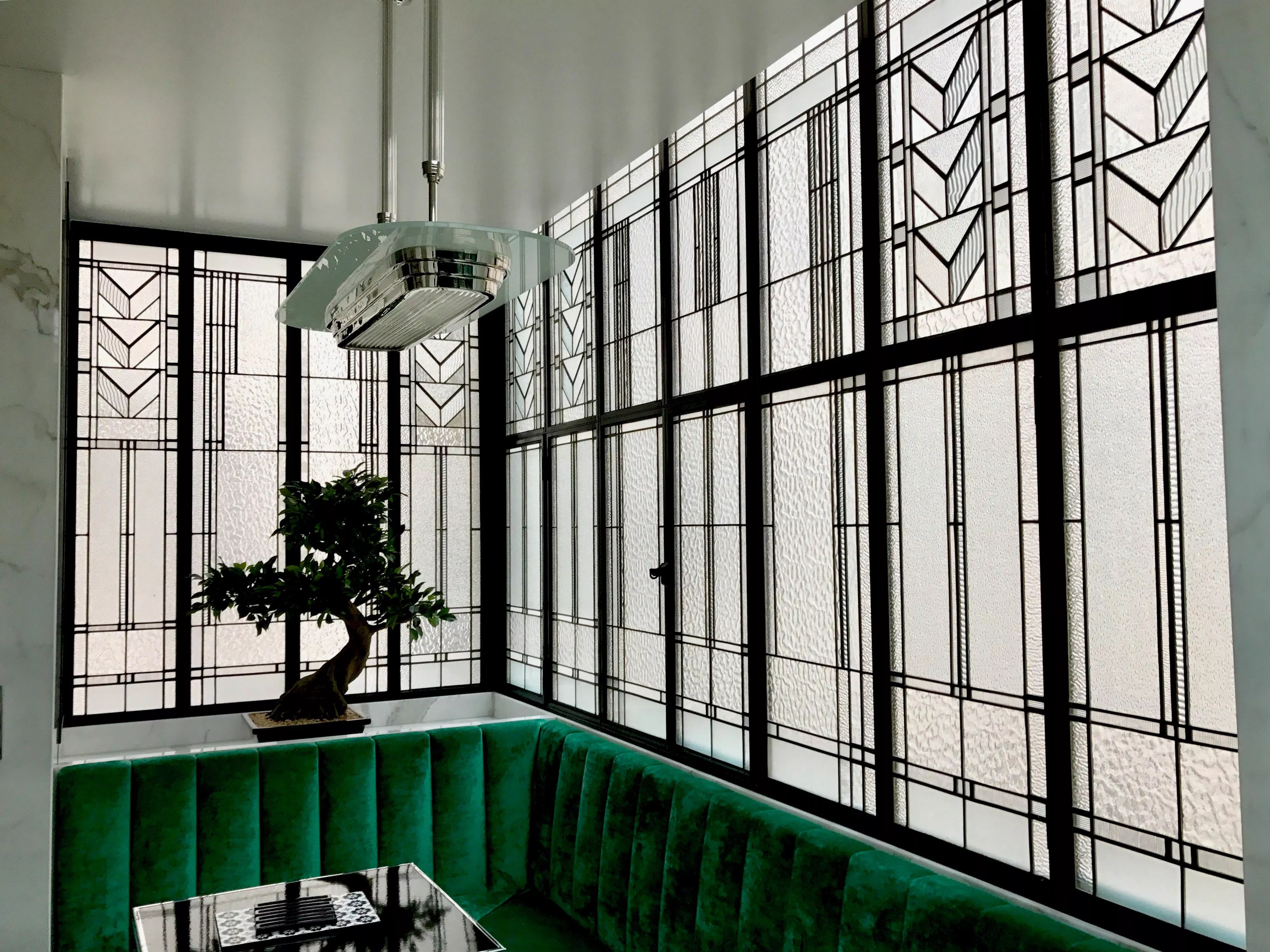 Décoration art déco en vitrail d'art sablé et gravé sur verrière d'angle noire par France Vitrail International, au-dessus d'une banquette en velours vert.