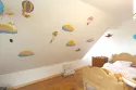 Fresque sur le mur en sous-pente d'une chambre d'enfant en Normandie, représentant un ciel avec des nuages et des animaux dans des engins volants,