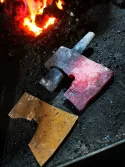 Un fer de hache et sa matrice à côté d'une forge