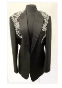 Veste de smoking agrémentée de fleurs argentées en crochet, entièrement réalisées à la main. Les motifs ornent les épaules et le haut du buste avant de se prolonger en délicates arabesques le long des côtés de la veste.