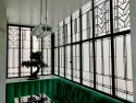 Décoration art déco en vitrail d'art sablé et gravé sur verrière d'angle noire par France Vitrail International, au-dessus d'une banquette en velours vert.