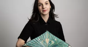 Lucie Le Goff, étudiante en DN MADE Marqueterie, posant avec son œuvre Éclosion, un éventail en marqueterie de paille et inserts de nacre